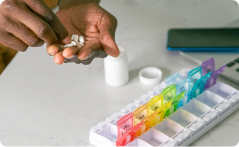 Hands placing pills into a weekly pill organizer.